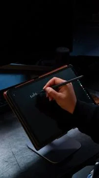 Hand using a digital pen on a tablet writing notes. Low light. Stock Photos