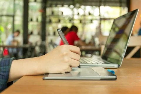 Hand using digital tablet and stylus penand working on laptop computer. Stock Photos