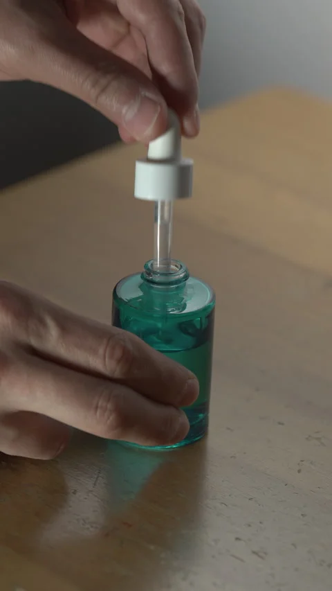 Hand Using Dropper Bottle of Blue Serum on Wooden Desk Stock Footage 312184242