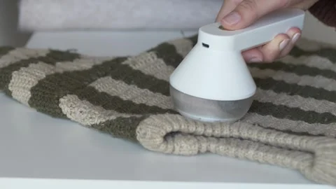 Hand using fabric shaver to remove lint from olive striped knit sweater on flat Stock Footage 331010465