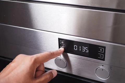 A hand is using a finger to activate the timer button on the control panel of a Stock Photos