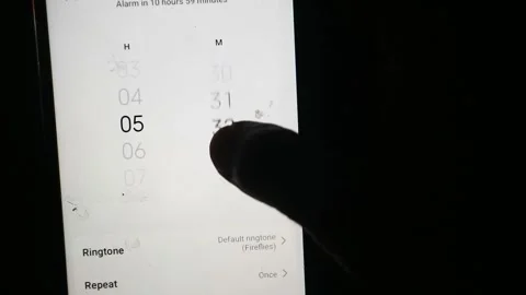 Hand using a finger to scroll and adjust the time setting on a smartphone Stock Footage 339304773
