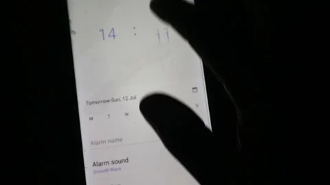 Hand using a finger to scroll and adjust the time setting on a smartphone Stock Footage 339304774
