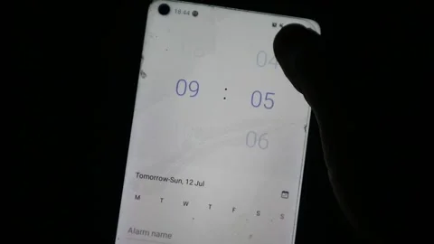 Hand using a finger to scroll and adjust the time setting on a smartphone Stock Footage 339304800