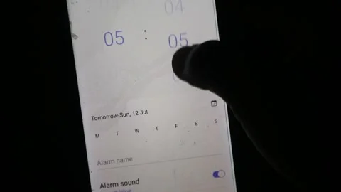 Hand using a finger to scroll and adjust the time setting on a smartphone Stock Footage 339304801