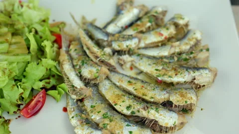 Hand using fork and knife, enjoying a delicious plate of grilled sardines with Stock-Footage 342857376