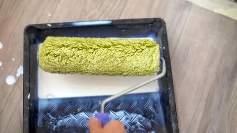 Hand using a green paint roller with white paint in a black tray during hom.. Stock-Fotos