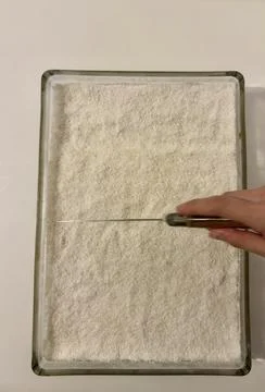 Hand using a knife to slice a rectangular coconut cake in a tray Stockfoto's