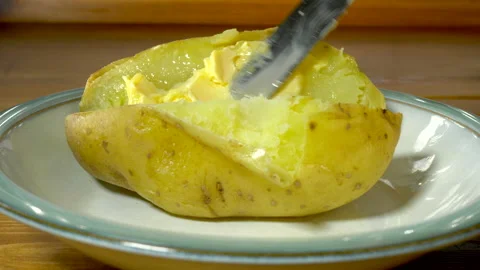 Hand using a knife to spread butter onto a hot baked potato. Stock Footage 167735898