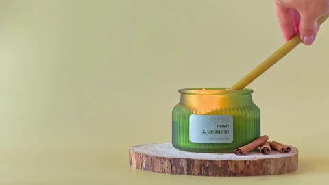 Hand using a long wax taper candle to light a candle in a ribbed green jar. Stock Footage 338026930