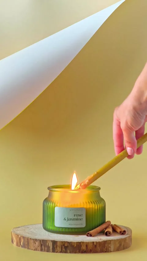 Hand using a long wax taper candle to light a candle in a ribbed green jar. Stock Footage 338026975
