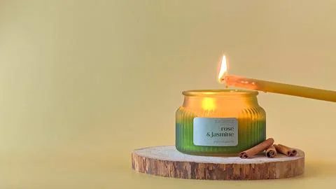 Hand using a long wax taper candle to light a candle in a ribbed green jar. Stock Photos