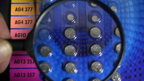 Hand using a magnifier / magnifying glass to see codes on button batteries. Stock Footage 164052479