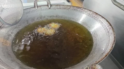 Hand using a mesh strainer to scoop food from a large frying pan. Stock Footage 342685833