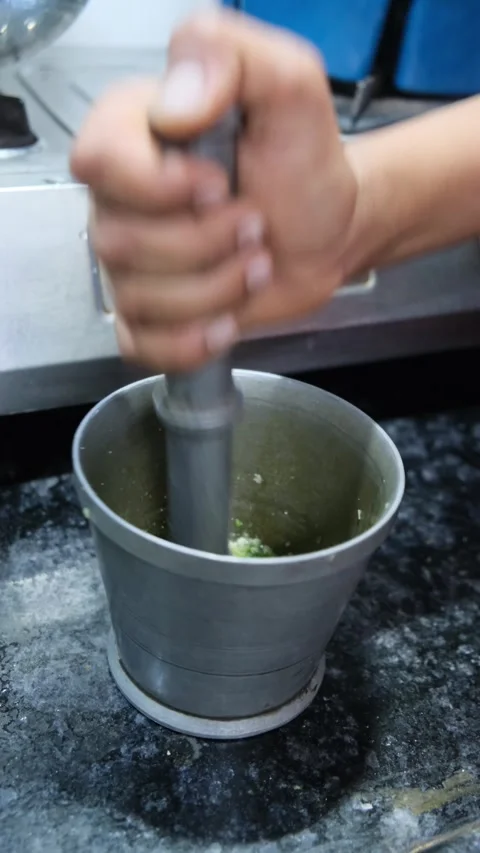 Hand using metal mortar and pestle to grind fresh green herbs in kitchen Stock Footage 331898839