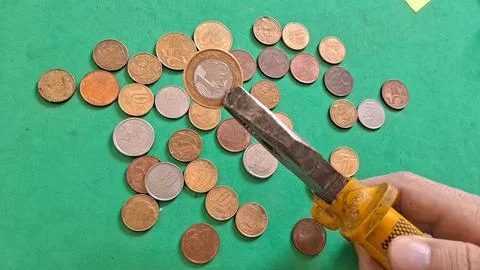 Hand using metal pliers to hold a single Brazilian real coin Stock Photos