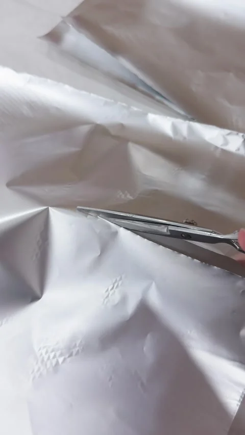 Hand using metal scissors for cutting a large sheet of shiny aluminum foil in Video stock 332824142