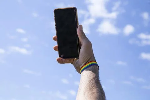 Hand up using the mobile with a lgtb colored bracelet with the sky in the bac Stock Photos