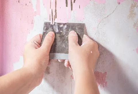 A Hand Using A Paint Stripper To Remove Old Paint From concrete wall. Stock Photos