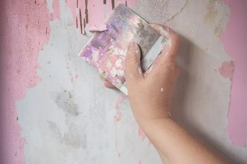 A Hand Using A Paint Stripper To Remove Old Paint From concrete wall. Stock Photos