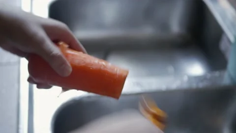 Hand using peeler to peel fresh carrot skin preparing for cooking Stock Footage 200390517
