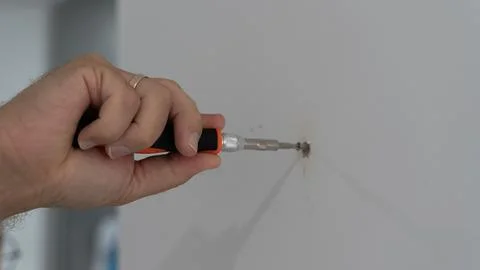 Hand Using Phillips Screwdriver to Tighten Screw in White Wall Photos