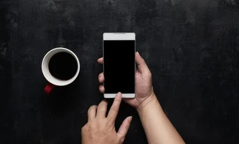 Hand using phone black screen with cup of coffee. Wooden black office desk ta Stock Photos