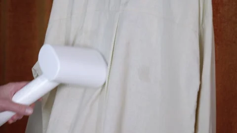 Hand using a portable garment steamer on a shirt Stockbeeldmateriaal 334322474