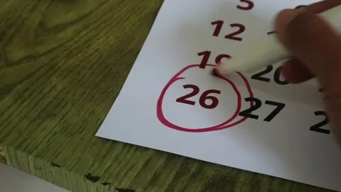 A hand using a red marker to circle the twenty-sixth day on a wall calendar Stock Footage 341956206