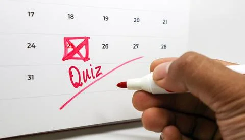 Hand using a red marker to write Quiz and cross out a date on a wall calend.. Stock Photos