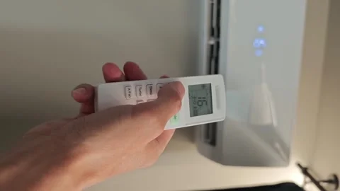 Hand using remote control to adjust air conditioner settings in a living room Stock Footage 342744096