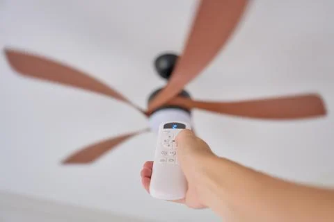 Hand using remote control to adjust ceiling fan speed in residential interior Stock Photos