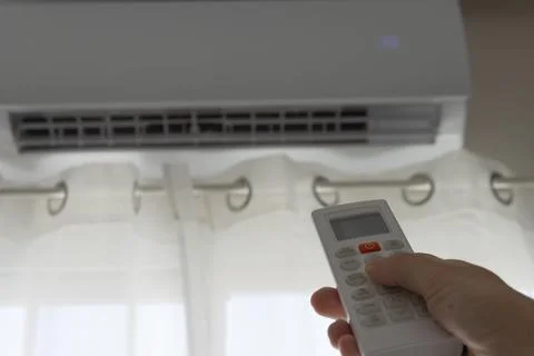 Hand using remote control operating air conditioning unit to adjust tempera.. Stock Photos