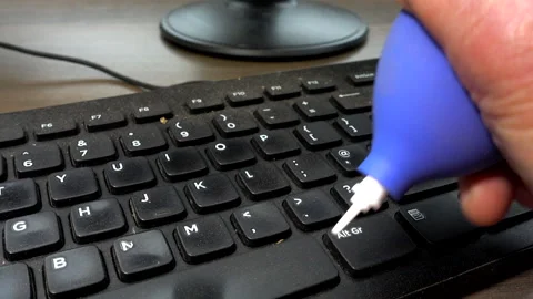 Hand using a rubber blower to remove dust from a computer keyboard. Video stock 200877569
