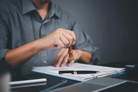 Hand using a rubber stamp on official papers, representing approval process.. Stockfoto's