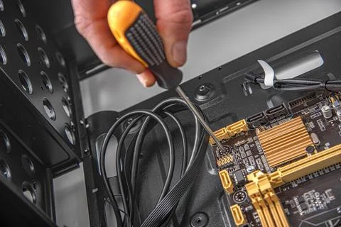 A hand using a screwdriver to install a motherboard into a computer case. Stock Photos