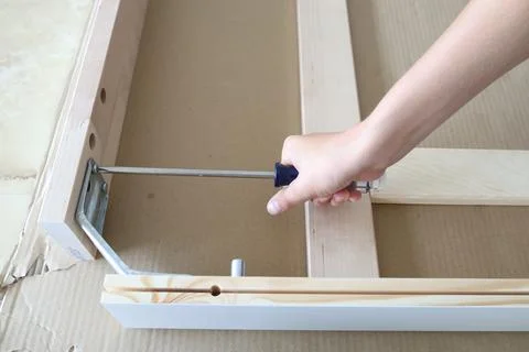Hand using screwdriver to secure wooden furniture structure with bracket Foto stock