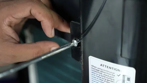 Hand using a screwdriver to tighten a screw on a black appliance panel, Han.. Stockbeeldmateriaal 338319458