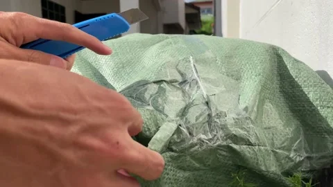 Hand using sharp cutter knife opening green sack filled with colourful ball foam Stock Footage 207727065