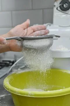 Hand using sieve to sift flour into yellow bowl. Household baking process s.. Stock Photos