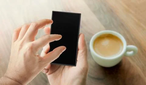 Hand using smart phone with cup of coffee on a wooden table on the background Stock Photos