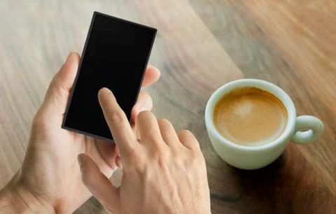 Hand using smart phone with cup of coffee on a wooden table on the background Stock Photos