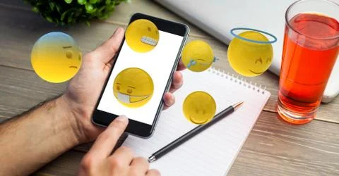 Hand using smart phone while emojis flying over table Stock Photos