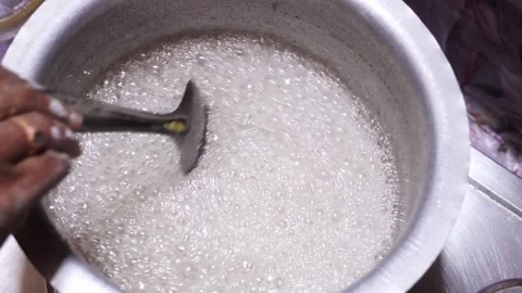 Hand using spoon to stir foaming hot sugar syrup boiling in metal pot. Vídeo Stock 346117840