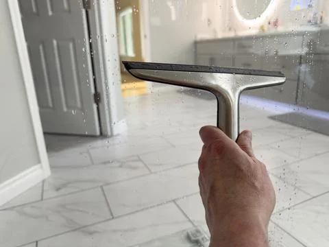 Hand using stainless steel squeegee to clean glass after taking a shower in.. Stock Photos