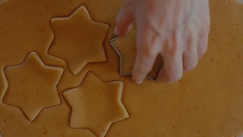 Hand using a star-shaped cookie cutter to press shapes into brown cookie dough Stock Footage 301276154