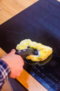 Hand using a steam cleaner with a microfiber cloth to clean a kitchen stovetop. Stock Photos