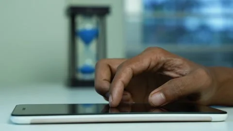 Hand using tablet beside blue sand timer, Close-up of a hand using a tablet.. Video stock 346484323