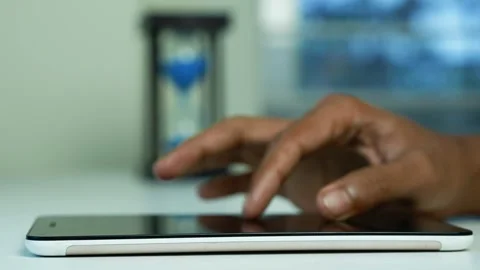 Hand using tablet beside hourglass, Close-up of a hand touching a tablet sc.. 스톡 동영상 346484340