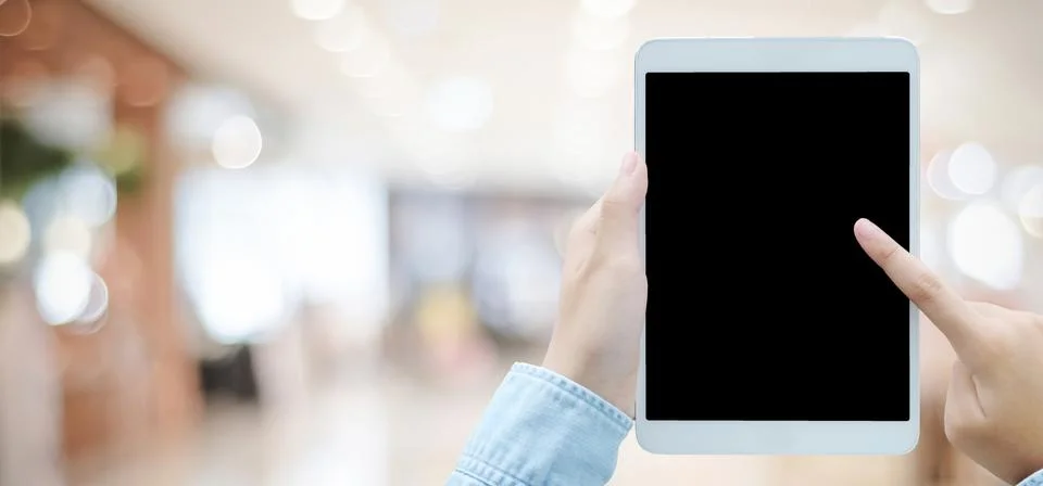 Hand using tablet with blank screen for mock up over blur store background Foto stock